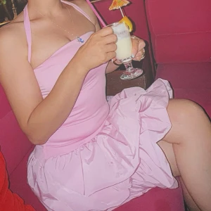 Ljusrosa kort klänning med volang - Supersöt ljusrosa kort klänning med halterneck och volangig kjol. Klänningen är ärmlös och har en tight passform upptill med en fluffig kjoldel. Perfekt för sommarens alla tillfällen när du vill sticka ut lite extra.