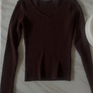Mörkbrun ribbad långärmad tröja - Snygg mörkbrun ribbad tröja från Punto Blanco med v-ringad hals och lång ärm. Tight passform som sitter riktigt snyggt och passar perfekt till jeans eller kjol. Enkel men stilren design som funkar året runt.