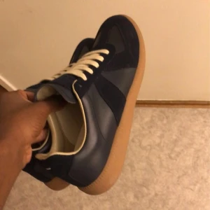 Mason margiela - Snygga mörkblå sneakers från mason margiela  med beige snörning och gummisula. Ovandelen är en mix av mocka och skinn, vilket ger en schysst kontrast. Klassisk rund tå och låg profil, perfekta för en clean och stilren look. Helt ny