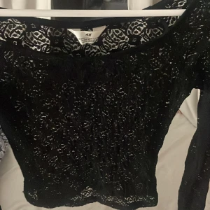 Svart spetsblus från H&M - Säljer en svart långärmad blus från H&M i genombruten spets med snyggt mönster. Toppen har rund halsringning och är figurnära, perfekt för dig som gillar detaljerad och elegant stil. Passar dig som vill sticka ut med en cool och trendig look. Endast använd några få gånger,gillade inte riktigt mönstret🩷