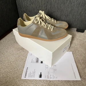 Maison Margiela Gats med Verifikation  - Maison Margiela sneakers i khaki/oliv med ovandel i skinn och mocka, klassisk gummisula och vita snören. Snygg retrostil med rund tå och diskreta detaljer. Perfekta för dig som gillar minimalistisk och stilren design. Köpta från vinted med verifikation och har därmed både kvitto och inspection label som äkthetsbevis. Ett av dem få paren som är äkta på plick. Kartong och dustbags ingår också.