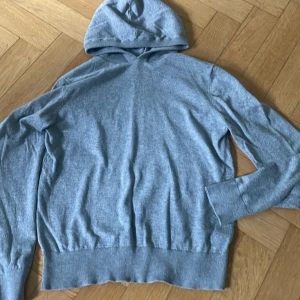 Ljusgrå hoodie från Grunt - Säljer en stilren ljusgrå hoodie från Grunt i storlek M. Tröjan har huva, långa ärmar och breda ribbade muddar vid ärmslut och nederkant. Perfekt för dig som gillar en enkel och clean look.