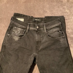 Svarta Replay Anbass jeans  - Säljer ett par svarta Replay Anbass jeans i slim fit. Jeansen har klassiska snygga slitningar och Replay-logga på fickan. Tillverkade i stretchigt jeansmaterial för en bekväm passform. Aldrig använda pga för små, 10/10 skick!