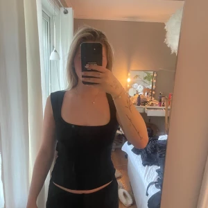 Svart linnetopp med fyrkantig hals Nelly - Svart linnetopp från Nelly i storlek XS. Toppen har en snygg fyrkantig halsringning och breda axelband som ger en stilren look. Modellen är figurnära och ärmlös, perfekt att matcha med jeans eller kjol. Materialet känns mjukt och stretchigt mot huden.