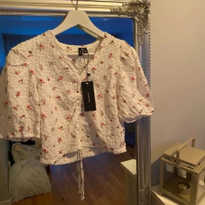 Vit blommig croppad blus med snörning - Supersöt vit blus med små rosa blommor och puffiga korta ärmar. Toppen är croppad och har snörning framtill som ger en snygg rynkad effekt. Ny med prislapp 🌸