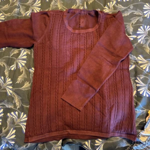 Mörkbrun stickad långärmad tröja - Snygg mörkbrun stickad tröja med lång ärm och rund hals. Framsidan har ett stilrent kabelstickat mönster och baksidan är slät med tre knappar upptill. Perfekt för dig som gillar klassisk stil med en twist.