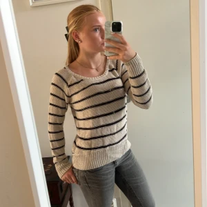 Randig stickad tröja från Lindex - Säljer en beige stickad tröja från Lindex i storlek S (men passar på mig som vanligtvis har XS). Tröjan har svarta horisontella ränder, rund halsringning och långa ärmar. Perfekt för dig som gillar en klassisk och avslappnad stil.