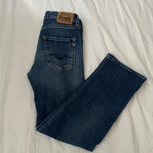 Blå Replay jeans straight fit - Snygga blå jeans från Replay med klassisk femficksdesign och raka ben. Jeansen har en mörk tvätt med lätt slitning, läderpatch bak och tydliga sömmar. Perfekta för dig som gillar en enkel men stilren look priset kan diskuteras.