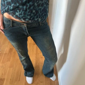 Blå gröna bootcut jeans med nitar  - Säljer ett par blå bootcut jeans från LIPS med låg midja. Jeansen har coola nitar och gröna toner. (några bitar har gått av, se bild 3) Storlek 29, innebenslängd 86cm och midjemått 38cm (rakt över).