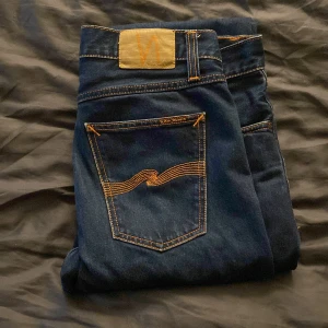 Mörkblå jeans från Nudie Jeans - Snygga mörkblå jeans från Nudie Jeans med klassisk femficksdesign och kontrastsömmar i orange. Jeansen har raka ben, har normal passform och är använda fåtal gånger. W32/L32. Pris är 700 men kan diskuteras