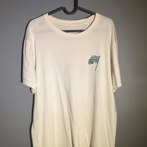 Bajen Forever t-shirt i bomull - Vit t-shirt med grönt tryck på bröstet och stor illustration på ryggen med texten 'Bajen Forever' och supporter-motiv. Klassisk rund hals och korta ärmar. Perfekt för dig som älskar Hammarby och vill visa ditt stöd på läktaren.