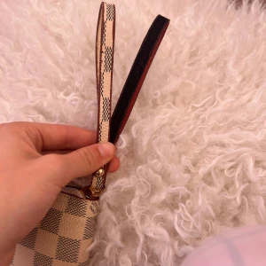 Rutig plånbok ni ser märket  - Snygg plånbok i klassiskt beige och grått rutigt mönster. Utsidan är i skinn med guldfärgade metalldetaljer och avtagbar handledsrem. Insidan är ljusblå med flera kortfack och dragkedjeförsett myntfack. Perfekt för dig som vill ha både stil och funktion. Och det är äkta skinn