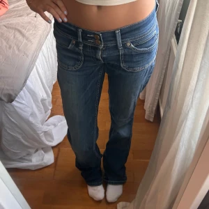 Blå bootcut jeans med låg midja - Säljer ett par blå jeans med snygg bootcut och låg midja. Jeansen har dubbla knappar, markerade sömmar och coola fickdetaljer både fram och bak. Perfekta för dig som gillar en avslappnad men trendig look.