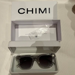 Grå transparenta solglasögon CHIMI - Snygga solglasögon från CHIMI i transparent grått acetat. Modell 04 och är fyrkantig med breda skalmar och mörka linser. Kommer med originaletui och box. Perfekta för dig som vill ha en clean och modern look.