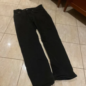 Svarta Levi's 501 jeans 34/32 - Svarta Levi's 501 jeans i klassisk rak modell. Jeansen har fem fickor, knappgylf och den ikoniska röda Levi's-taggen på bakfickan. Tillverkade i slitstarkt jeanstyg som ger en tidlös look. Perfekta för dig som gillar en clean och enkel stil. Liten prick färg på högra höften men så liten att man knappt märker den.