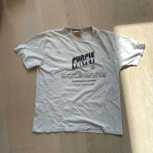 Vit t-shirt från Eytys med tryck - Säljer en vit t-shirt från Eytys i storlek M med svart grafiskt tryck på bröstet där det står 'Purple Velvet'. T-shirten har rund hals och korta ärmar, tillverkad i mjuk bomull. Perfekt för dig som gillar coola statement-plagg och streetwear.