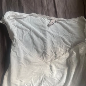 Vit v-ringad linnetopp från Nelly - Supersöt vit linnetopp från Nelly i storlek XS. Toppen har v-ringning och fina spetsdetaljer längs kanten som ger en romantisk vibe. Perfekt att styla med jeans eller kjol för en fräsch look.
