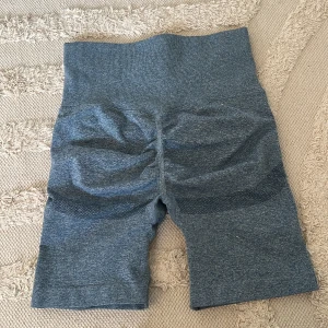 Blå träningsshorts med scrunch  - Säljer ett par blå seamless träningsshorts med hög midja och ribbad kant. Materialet är stretchigt och består av polyamid, polyester och elastan. Perfekta för gymmet eller andra sportaktiviteter. Snygg scrunch-detalj bak för extra passform.
