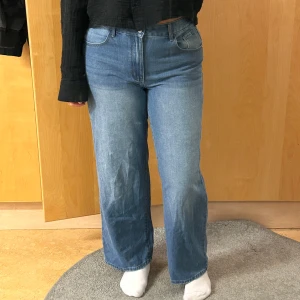 Blå wide jeans med hög midja - Säljer ett par blå jeans med hög midja och wide fit. Jeansen har klassisk femficksdesign, knapp och dragkedja fram samt raka, breda ben. Materialet är jeans i bomull och färgen är ljusblå med lite tvättade detaljer. Perfekt för dig som gillar avslappnad stil.
