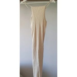 Beige ribbad långklänning från Zara - Supersnygg ribbad långklänning från Zara i beige/vit färg med smala axelband som korsas i ryggen. Klänningen är figurnära och har en stilren, minimalistisk look. Perfekt för dig som gillar enkel men trendig stil.