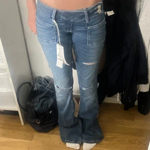 Blå flare jeans från Gina Tricot XXS - Snygga blå flare jeans från Gina Tricot i modellen 14+ pleated flare. Låg midja, bootcut och slitna detaljer vid knäna. Stora fickor fram och dubbla knappar i midjan.