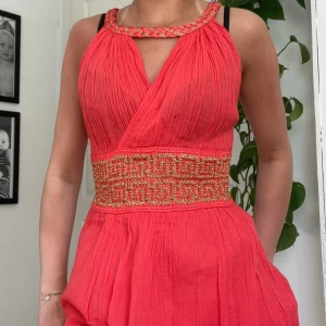 Röd klänning med gulddetaljer - Jättefin röd klänning köpt förra året på Kreta. Det står ingen storlek men jag har vanligtvis xs så jag uppskattar denna till en xs. Nästan aldrig använd, därför säljer jag den. Klänningen har 2 lager nertill vilket gör att den inte är genomskinlig. 