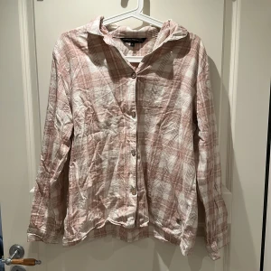 Rutig rosa pajamas skjorta från Pernilla Wahlgren - Säljer en rutig pyjamasskjorta i ljusrosa och vitt från Pernilla Wahlgren. Skjortan har klassisk krage, knäppning framtill med knappar och långa ärmar. Mysig att sova i.