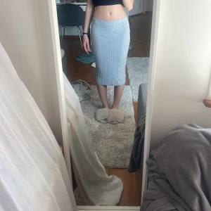 Grå ribbad kjol  - Säljer en grå, ribbad midilång kjol från H&M Divided i storlek XS. Kjolen är figurnära och har en stretchig känsla som sitter snyggt på kroppen. Perfekt att styla med en crop top eller hoodie för en chill look. Lite nopprig men inget man tänker på