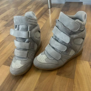 Nya Isabel Marant-liknande skor i mocka. - Snygga grå sneakers med inbyggd kilklack och breda kardborreband. Skorna är gjorda i mjuk mocka och har en cool, sportig design med perforerade detaljer på tån och vadderad kant. Perfekta för dig som vill ha lite extra höjd men ändå en streetstyle-look. Inte äkta Isabel Marant skor men ser exakt ut som det! Skorna ser helt NYA ut och det finns inga täcken på användning. Säljer då dem inte passar 💕💕
