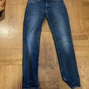 Levi's 511 blå jeans 28/32 - Säljer ett par klassiska Levi's 511 jeans i mörkblå tvätt med snygga slitningar. Modellen är slim fit med raka ben och normal midja. Jeansen har fem fickor, gylf med dragkedja och den ikoniska Levi's-lappen bak i brunt läder.
