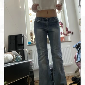 Blå bootcut jeans med låg midja - Säljer ett par blå bootcut jeans med låg midja och klassiska fickor fram och bak. Jeansen har en lätt tvättad look och subtila vertikala sömmar som ger en snygg vintagekänsla. Perfekta för dig som gillar 00-talsstil!