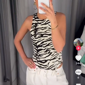 Zebramönstrad ärmlös body - Snygg ärmlös linnetopp med zebramönster i svart och vitt. Toppen har rund halsringning och sitter tight mot kroppen, perfekt för att sticka ut med en trendig look. 