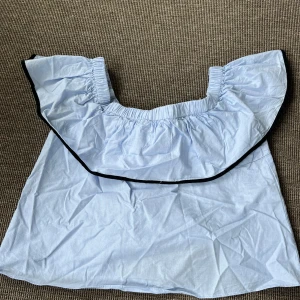 Ljusblå offshoulder topp från Zara - Supersöt ljusblå offshoulder topp från Zara med volang runt axlarna och svarta detaljer. Toppen har en svart knytning i ryggen, vilket också gör den supersöt! Perfekt för dig som vill se fin ut nu i sommar!!