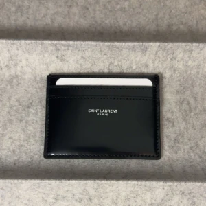 Saint Laurent plånbok - Ysl plånbok/korthållare Ny, aldrig använd. Medföljer certifiering av äkthet. Glansig svart färg. Ny pris runt 3000kr