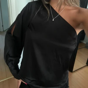 Svart oneshoulder blus i satin - Säljer en svart oneshoulder blus i satin material. 