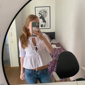 Vit blus med knyt från H&M Divided - Supersöt vit blus från H&M Divided i luftig bomull. Modellen är croppad med volang nertill, korta ärmar och snygg knytning framtill som ger en chill och trendig vibe. Perfekt till jeans eller kjol för en fräsch look.