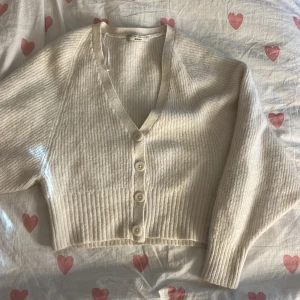 Vit stickad kofta från Gina Tricot - Superfin vit stickad kofta från Gina Tricot med v-ringning och stora knappar framtill. Modellen har långa ärmar. Perfekt att slänga över en topp för en chill och snygg look.