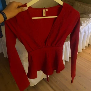 Röd topp med knyt i ryggen - Säljer en röd omlottopp från Nelly med v-ringning och långa ärmar. Toppen har en söt knytning i ryggen och lätt rynkad struktur i tyget. Perfekt för dig som vill ha en färgstark och trendig look.❤️ hör av er vid frågor❤️ pris går att diskutera❤️