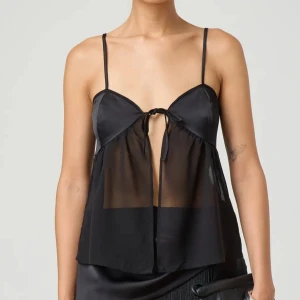 Svart transparent linnetopp med knyt - Supersnygg svart linnetopp med tunna axelband och transparent tyg. Toppen har en söt knytning framtill och är luftig med en loose passform. Perfekt för dig som vill sticka ut med en trendig och cool look. Fest topp. Skit snygg. Aldrig använd.