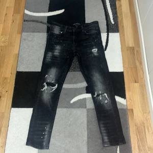 Svarta jeans från Supply & Demand - Snygga svarta jeans från Supply & Demand med slitna detaljer och en cool, tvättad look. De har en klassisk femficksdesign och knappgylf. Perfekta för en avslappnad stil med en edgy touch. Byxorna är också helt nya köpte några månader sen från JD store och har används 3-4 gånger. De är som nya och de är inte slitna och har inga skador eller slitningar. De är köpta för 350 och jag säljer dom för 200 men priset kan såklart diskuteras.