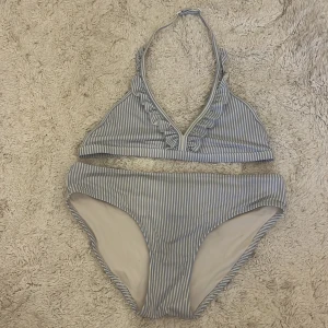 Blåvit randig bikini med volang - Superfin bikini från Lindex med blåvita ränder och volangdetaljer på överdelen. Bikinin har en halterneck-topp med djup v-ringning och knäppning i ryggen. Underdelen är klassisk med medelhög midja. Perfekt för stranden eller poolen!