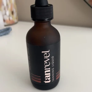 Tanrevel Tanning Liquid 60 ml - Tanrevel Tanning Liquid i en brun glasflaska med svart pipettlock. Innehåller 60 ml brun-aktig vätska som ger en solkysst look. Passar perfekt för att få en jämn och naturlig bränna utan sol. Flaskan har stilren svart etikett med vita och kopparfärgade detaljer.