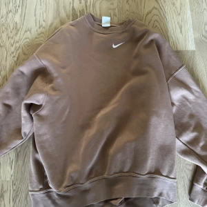 Brun sweatshirt från Nike - Säljer en brun sweatshirt från Nike med klassisk vit swoosh på bröstet. Tröjan har rund hals, långa ärmar och en relaxed passform. Perfekt för en chill och sportig stil. Materialet är mjuk bomullsmix som känns skön mot huden.