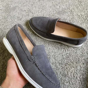 Grå mockaloafers med vit sula - Snygga loafers i grå mocka med stilren design och vit platt sula. Skorna har en klassisk rund tå och är perfekta för en clean och avslappnad look. Passar till både jeans och chinos för en chill vibe.