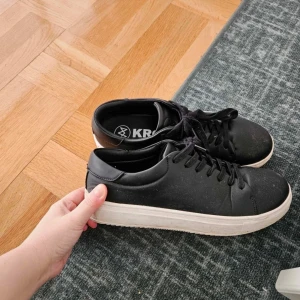 Svarta sneakers från KRONSTADT - Stilrena svarta sneakers från KRONSTADT med vit platt sula och klassisk snörning. Skorna har en minimalistisk design och är tillverkade i syntetmaterial. Perfekta för en clean och modern look. Storlek 44. Använda fåtal gånger så har mycket mer att ge.