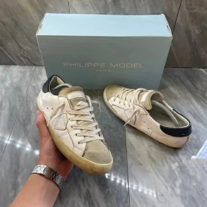 Philippe Model vita sneakers i skinn - Snygga vita sneakers från Philippe Model med beige mockadetaljer på tån och plös, samt svart hälparti. Skorna har klassisk snörning och en slitstark gummisula. Perfekta för dig som gillar stilrena och trendiga sneakers med exklusiv känsla.