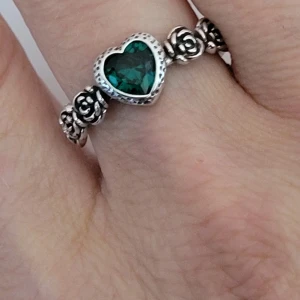  Helt ny Silverring 925 med hjärta och rosor -  Helt ny Superfin silverring i 925 sterling silver med ett grönt hjärtformat stenhänge i mitten. Ringen har detaljerade små rosor runt hela bandet som ger en romantisk vibe. Perfekt för dig som gillar unika smycken med lite extra känsla. Justerbar kommer passa de flesta fingrar 