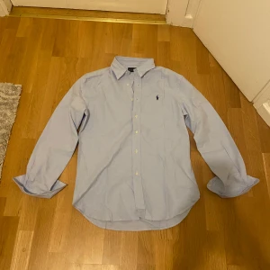 Ljusblå skjorta från Ralph Lauren S - Klassisk ljusblå skjorta från Ralph Lauren i storlek S. Skjortan har button-down krage, långa ärmar och knappar framtill. Broderad logga på bröstet. Tillverkad i mjuk bomull som känns skön mot huden. Perfekt för en clean och stilren look. Storlek S men passar M mer, helt ny inga tags 
