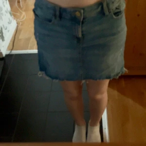 Blå jeanskjol med fransig kant Lindex - Säljer en klassisk blå jeanskjol från Lindex med fransig nederkant och femficksmodell. Kjolen  har knappstängning framtill. Perfekt för en avslappnad stil. Skriv vid frågor och för fler bilder💕💕