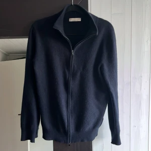 Kashmir tröja - Snygg mörkblå kofta från Luca Faloni i lyxig kashmir. Tröjan har hel dragkedja framtill, hög krage och ribbade muddar. Perfekt för dig som gillar stilrena och klassiska plagg med premiumkänsla. Passar runt 165 till 172